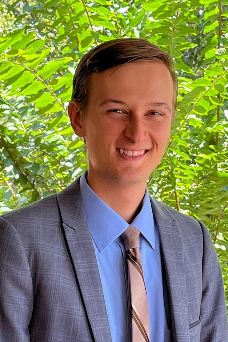 Portrait headshot of a male student standing in front of a light grey background, smiling at the camera. 