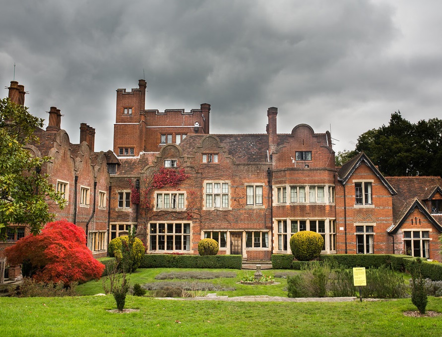 Old brick buildings of Newbold College with bright red tree and stormy sky.
