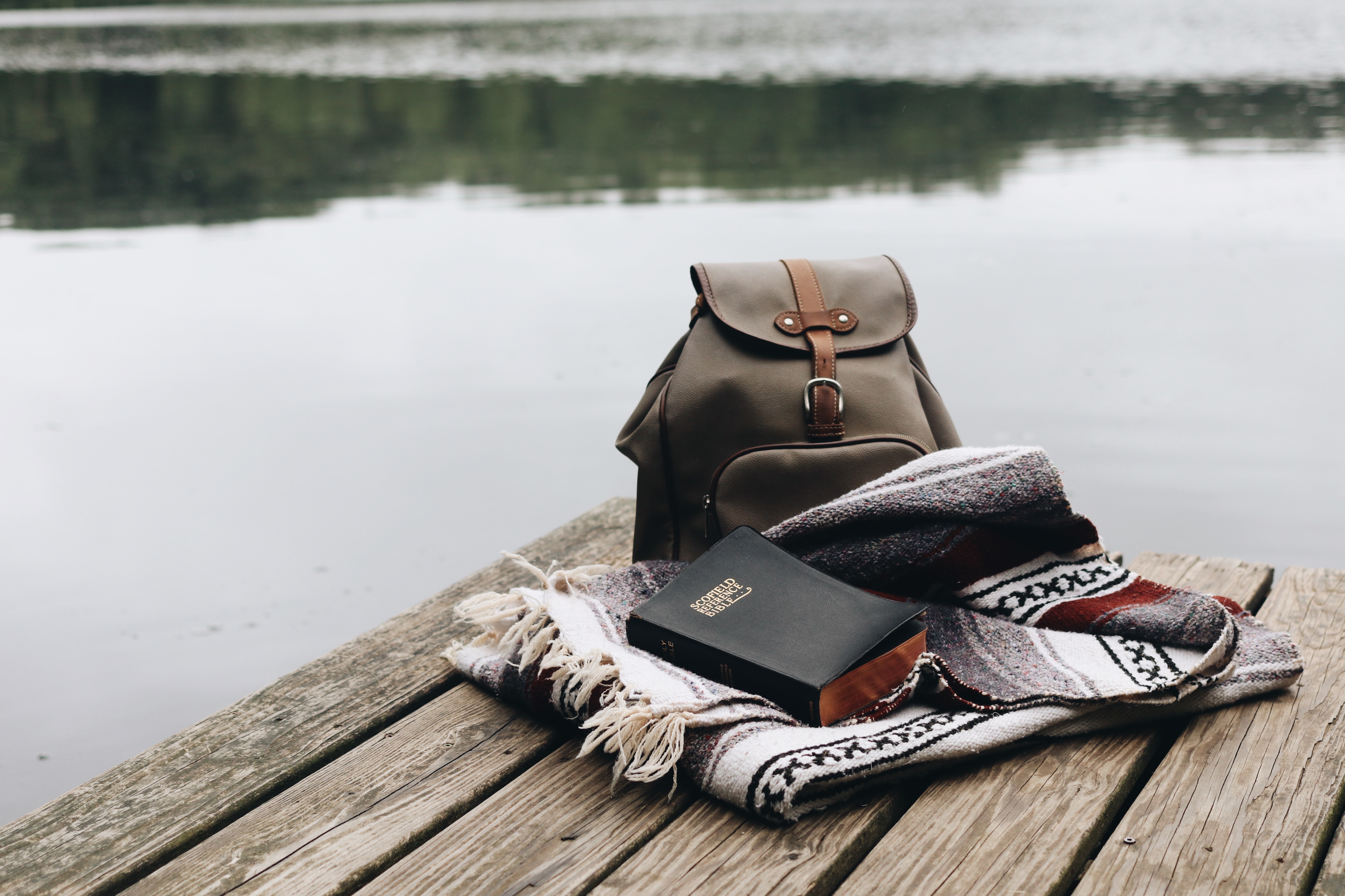 Bible and journal with backpack on a dock surrounded by water