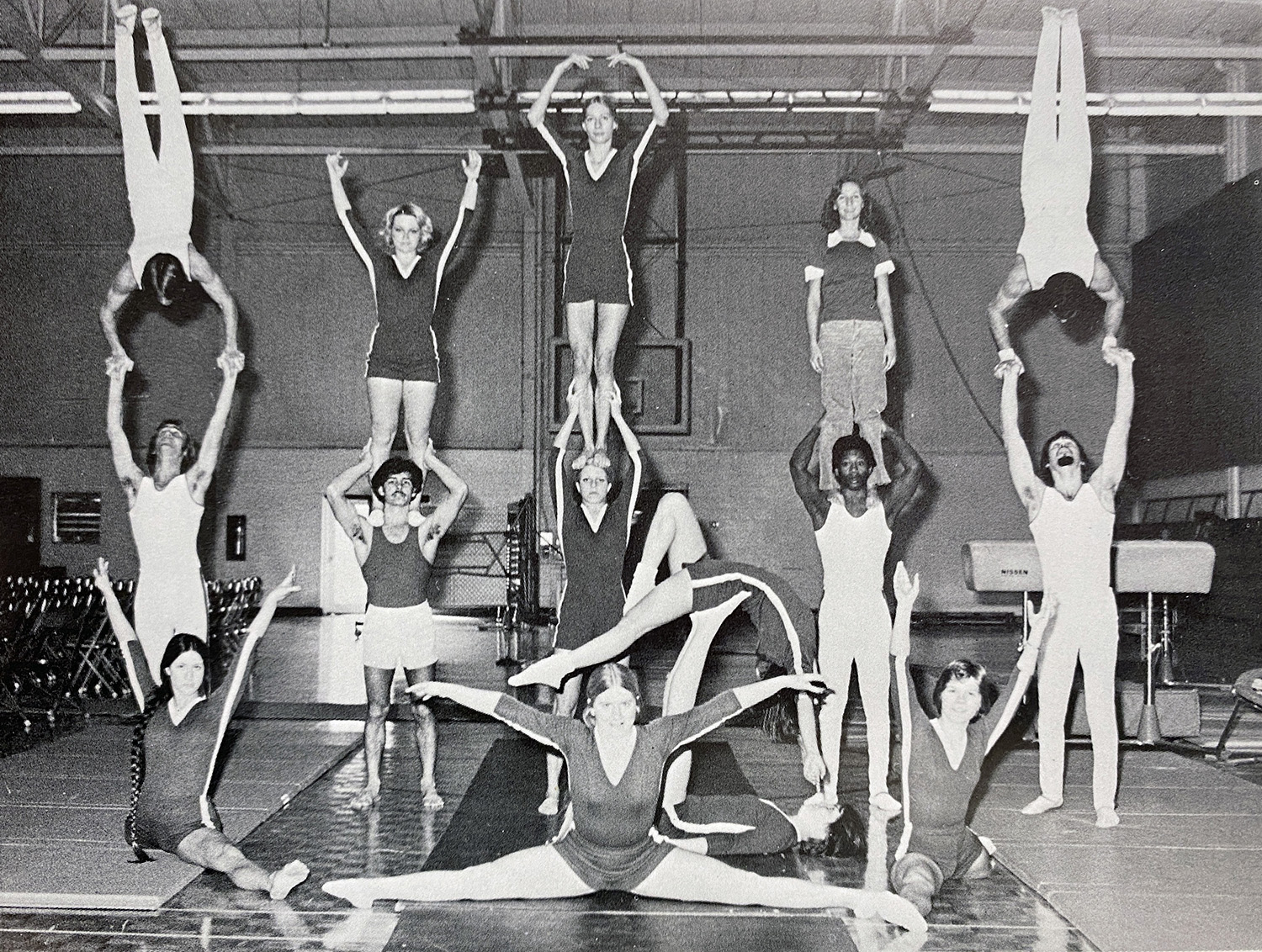 A black and white photo of the Gym-Masters team of 1977 performing a variety of skills and tricks posing for the camera.