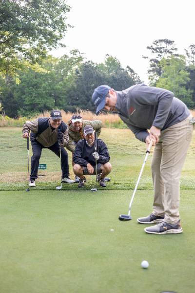 Three golfers watching one person putt