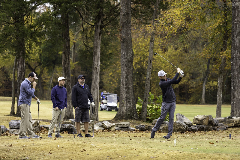 three people watching someone hit a golf ball