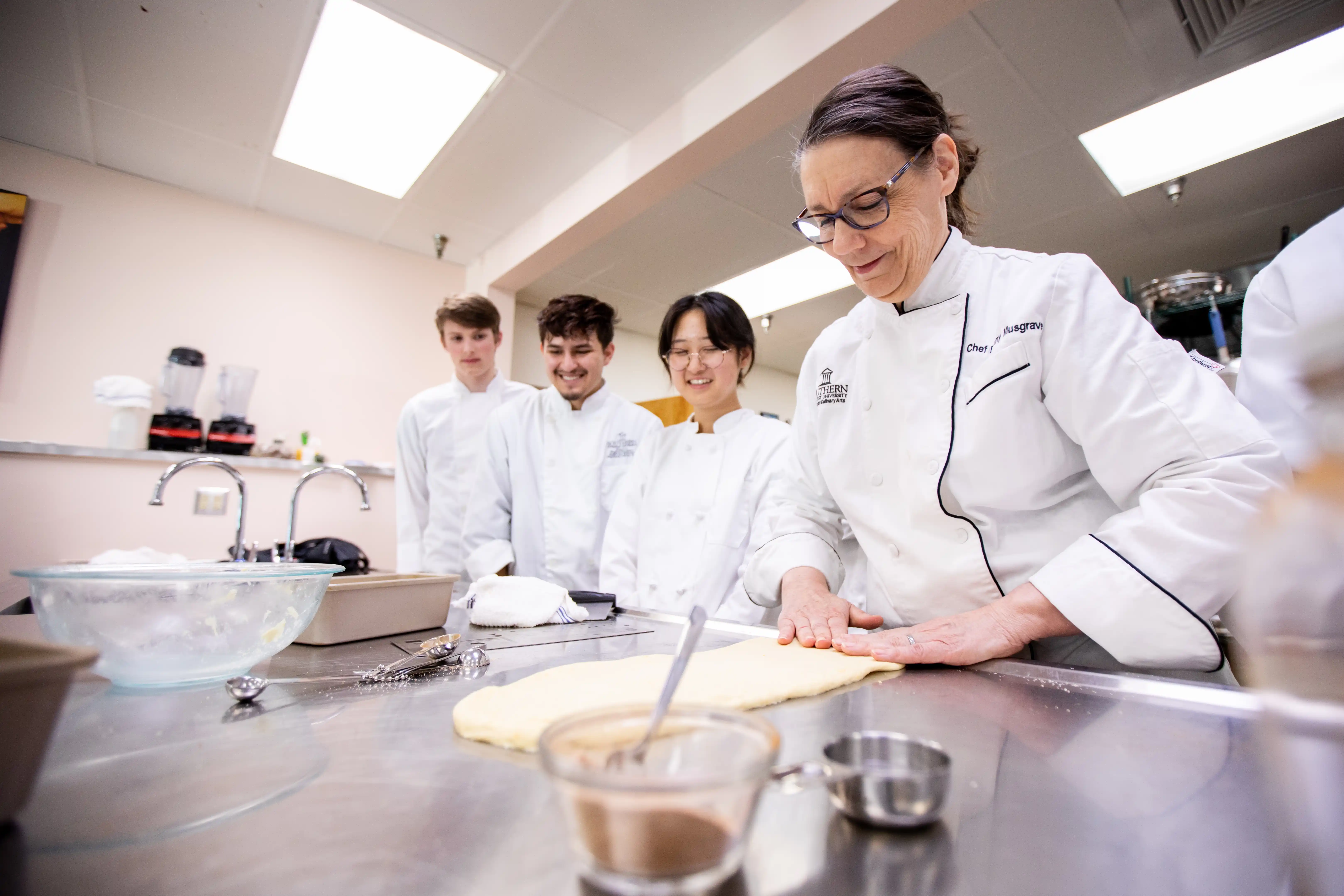 Three Southern Culinary Arts students watching their instructor roll dough