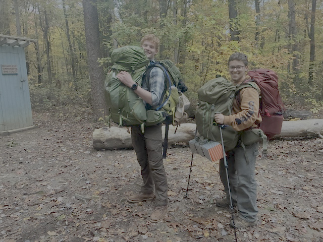two studenst carry multiple backpacks while rescuing an injured hiker